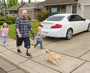 Man wearing prosthetic arm walking dog with young boy.