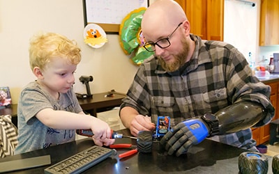 Man with prosthetic arm and young boy building toy together.