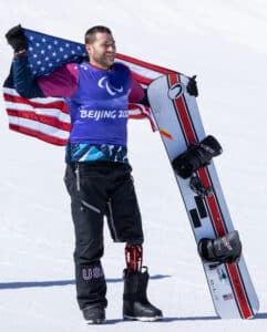 Mike Schultz stands with his snowboard in one hand and the American flag across his shoulders.