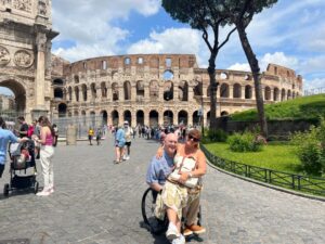 Man in wheelchair pictured with a woman sitting on his lap in front of the Colosseum.